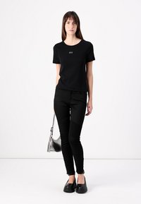 T-shirt en coton noir avec un col rond et le logo GAP. Un pantalon skinny noir avec des accents texturés et un sac à bandoulière argenté.