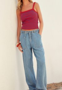 Czerwony i niebieski top na ramiączkach w paski, zestawiony z luźnymi, jasnoniebieskimi spodniami dżinsowymi z elastycznym pasem i bocznymi kieszeniami.