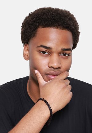Black chain bracelet with interlocking links displayed on a wrist, worn by a person with curly hair, set against a plain background.