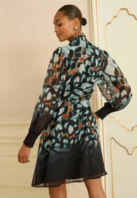 Rochie tip bluza cu maneci lungi, din material transparent, cu guler volănat, având modele abstracte în nuanțe de albastru, negru și portocalie; talie strânsă și fustă fluidă.