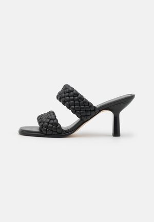Sandale mule noire à talon avec deux larges brides en cuir tressé et un talon de hauteur moyenne légèrement évasé sur un fond uni.