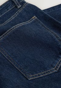 Tissu en denim bleu foncé avec une poche arrière présentant une couture orange et une partie d'une passants de ceinture sur un jean.