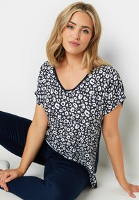 Top med leopardmönster i marinblått och vitt, med korta ärmar, V-ringning, avslappnad passform och mjukt tyg. Matchas med marinblå byxor.