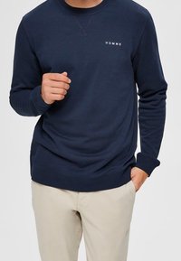 Námořnická mikina s kulatým výstřihem, žebrovanými manžetami a lemem. Obsahuje bílé logo "HOMME" na hrudi a má hladkou texturu.