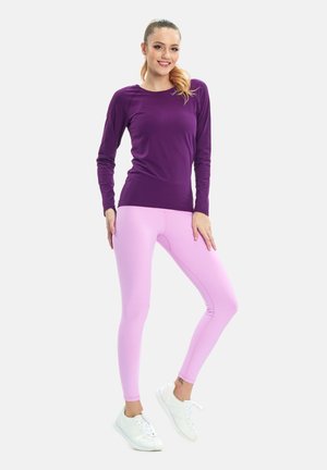 Paarse lange mouw top gecombineerd met lichtroze leggings. De outfit is gemaakt van soepel, rekbaar materiaal. Witte sneakers maken de look af.