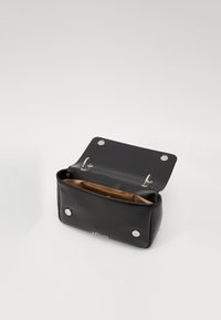 Black leather bag with a smooth texture, featuring a snap button closure and a tan interior. Interior has no additional pockets.