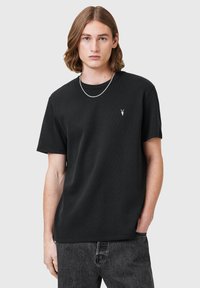 Camiseta negra de manga corta de algodón, con un logotipo sutil en el pecho. Textura suave, ajuste relajado, combinada con jeans de mezclilla oscura.