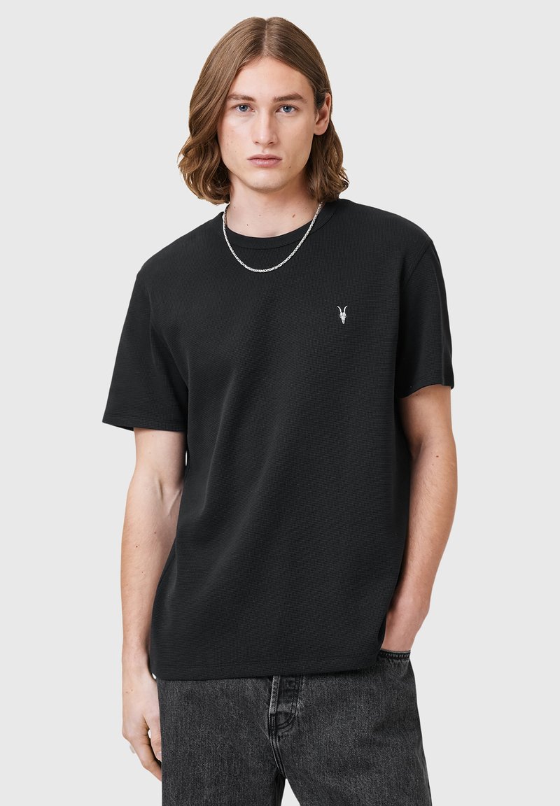 Camiseta negra de manga corta de algodón, con un logotipo sutil en el pecho. Textura suave, ajuste relajado, combinada con jeans de mezclilla oscura.