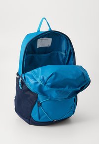 Mochila azul com uma base azul escura, bolso lateral em rede, um bolso interno e uma aba superior arredondada. Projetada para armazenamento versátil.