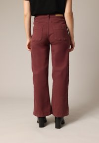 Jeans amples bordeaux en denim de coton, avec deux poches arrière, taille haute et texture lisse.