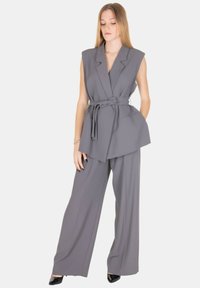 Gilet grigio su misura e pantaloni a gamba larga, realizzati in tessuto liscio. Presentano una vita con cintura e spalle strutturate.