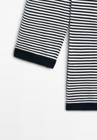 Sort og hvidt horisontalt stribet strikket stof med sorte ribstrikkede manchetter, der viser ærmedelene på en hvid baggrund.