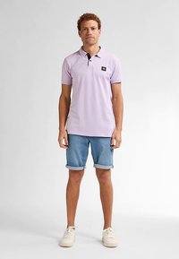 Světlofialová polokošile s krátkými rukávy, černý akcent u límce, v kombinaci s džínovými kraťasy s ohrnutými lemy a bílými teniskami.