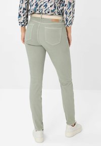 Hellgrüne Skinny Jeans aus Denim, ausgestattet mit zwei Gesäßtaschen und einem dezenten Logo-Patch. Getragen mit einem beigen Gürtel und weißen Sneakers.