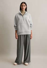 Grauer Fleece-Pullover mit einem halben Reißverschluss und Vordertasche, kombiniert mit weiten grünen Karohosen und cremefarbenem Schuhwerk. Einfaches, lässiges Outfit.