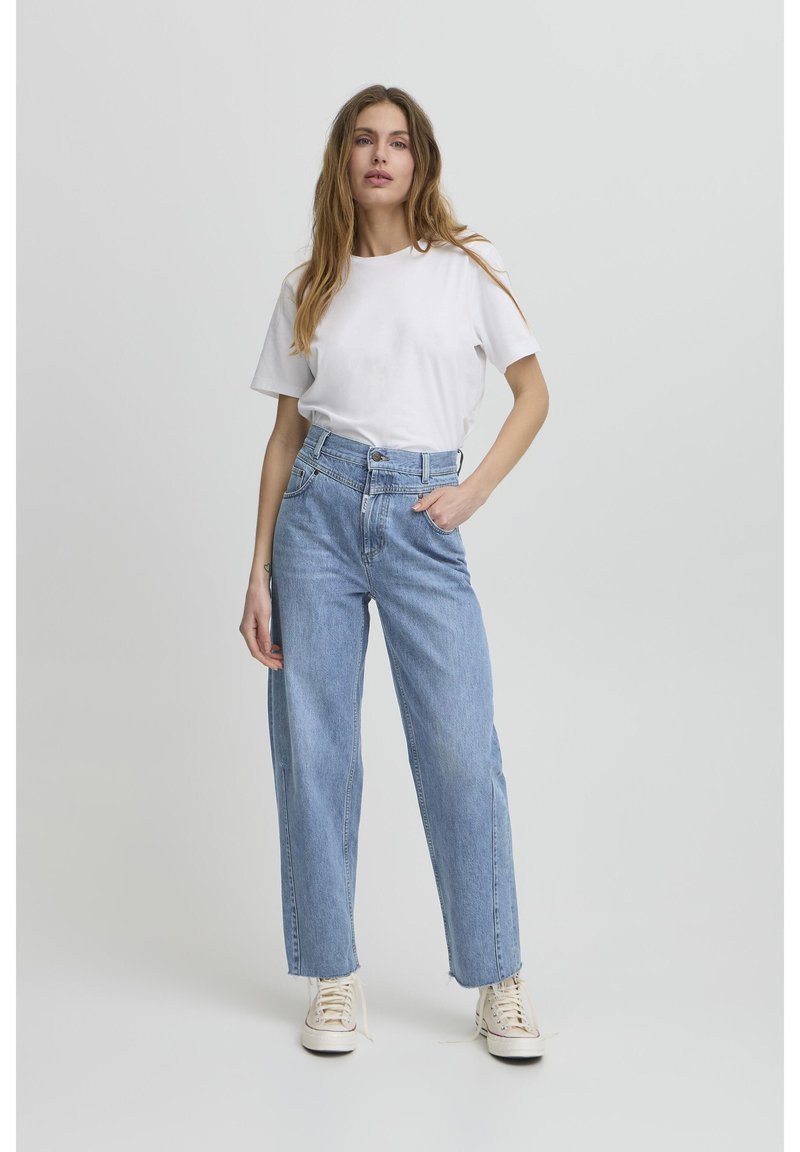Camiseta de algodón blanca combinada con jeans de mezclilla de tiro alto en un tono azul claro. Los jeans tienen un corte recto y un ligero deshilachado en el dobladillo.
