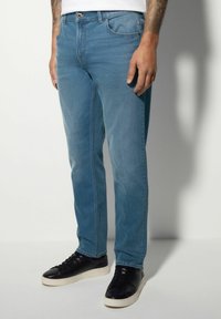 Svetlobluši jeans s ravnim krojem, petimi žepi in zadrgo. Obuti z črnimi supergami z belim podplatom.