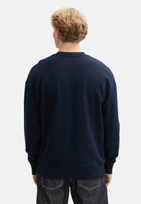 Sudadera azul marino con cuello redondo, mangas largas y puños acanalados. Textura suave, diseño casual y cintura ajustada.