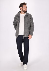 Grå zip-up jacka med hög krage, bärs över en vit t-shirt. Mörkblå jeans och vita sneakers fulländar outfiten. Avslappnad look.