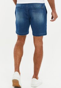 Shorts in denim blu scuro con una finitura sbiadita, dotati di due tasche posteriori e orlo dritto. Abbinati a sneakers bianche.