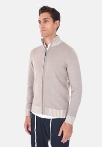 Maglione beige con zip, colletto e polsini a coste, realizzato in un morbido materiale, con una consistenza solida e un design aderente.
