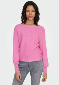 Rosa ribbestrikket genser med vid halslinning, lange ermer og avslappet passform. Kombinert med lysegrå jeans med myk tekstur.