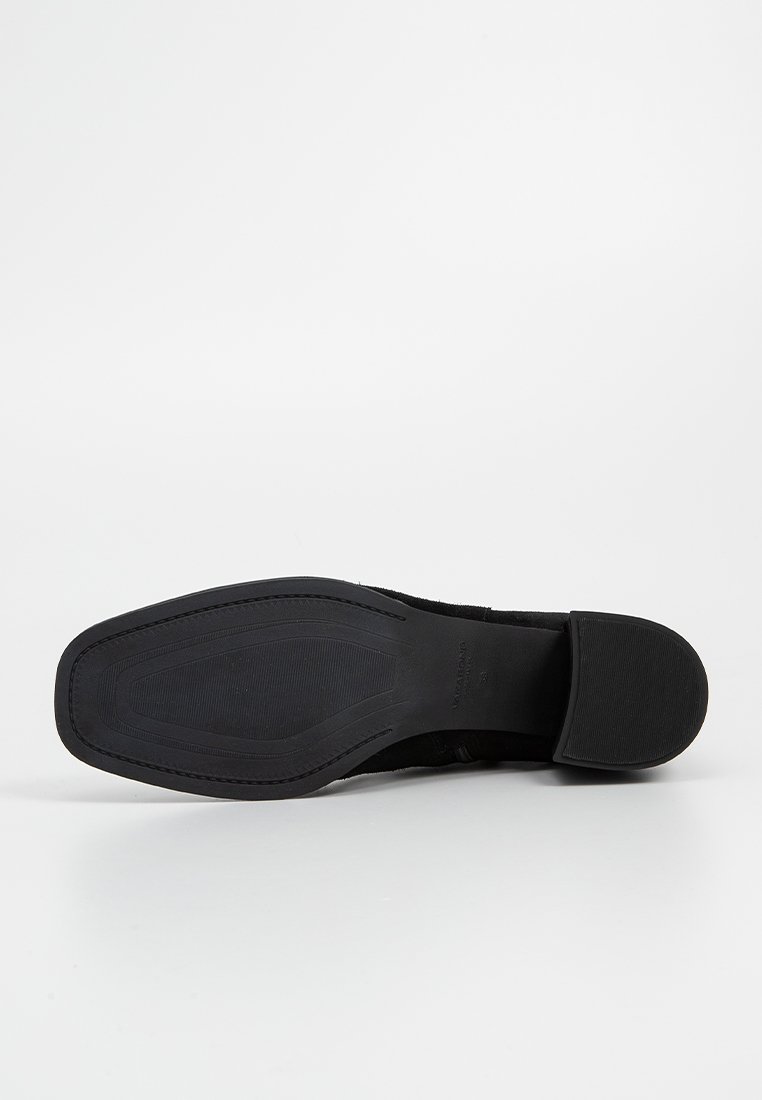 Schwarze Ledersohle mit flachem Design, strukturiertem Gummi für Grip und abgerundeten Kanten. Minimale Markenpräsenz auf der Unterseite.