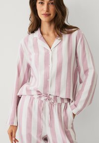 Ensemble de pyjama rayé en rose clair et blanc, comprenant un haut à col avec boutons et un pantalon à taille élastique avec cordon de serrage. Tissu doux et respirant.