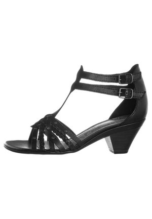 Sandales en cuir noir avec un design à sangle T, présentant des détails tressés et deux boucles ajustables. Le talon en bois bas ajoute de la stabilité.