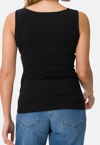 Top nero senza maniche con scollatura rotonda, design aderente e tessuto morbido, abbinato a jeans azzurri chiari con un classico design della tasca posteriore.