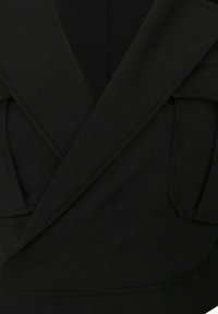 Gros plan sur un tissu noir montrant des revers structurés qui se chevauchent et un détail de poche avec des coutures visibles.