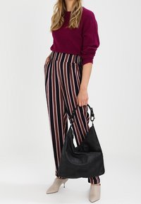 Musta olkalaukku, jossa on teksturoidun näköinen pinta, yhdistetty viininpunaiseen neulepuseroon ja mustavalko-pinkkiraitaisiin leveälahkeisiin housuihin.