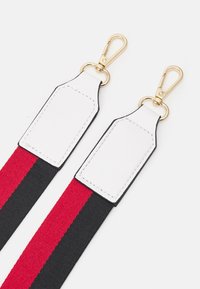 Punamustaraidallinen nailonremmi, jossa valkoiset nahkakohteet ja kullanväriset metallikiinnikkeet varmaa kiinnitystä varten.