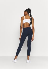Weiße Sport-BH und marineblaue Leggings. Die Leggings sind enganliegend und haben einen hohen Bund; beide bestehen aus glattem, elastischem Material und weisen minimale Details auf.