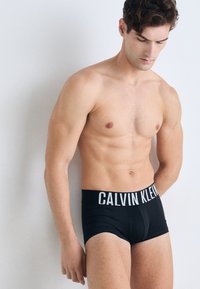 Schwarze Baumwoll-Boxershorts mit einem weichen Bund, auf dem "CALVIN KLEIN" in weißen Buchstaben steht; glatte Textur und taillierte Passform.