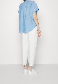 Blå och vit randig kortärmad skjorta med avslappnad passform, i kombination med vita smalare byxor och vita sneakers. Bakifrån.