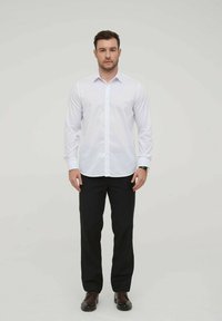 Chemise blanche à manches longues avec col pointu, associée à un pantalon noir. La chemise a une texture lisse et une coupe régulière.