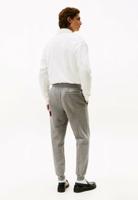 Sudadera blanca con cuello alto, combinada con pantalones de chándal gris ajustados que tienen bolsillos laterales y un detalle en rojo. Zapatillas negras completan el look.
