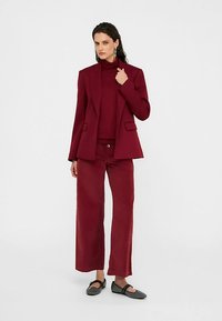 Bourgognefarvet blazer med hakflip, kombineret med en matchende rullekrave og vidde bukser, suppleret med sorte ballerinaer og sølvøreringe.