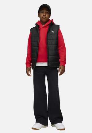 Gilet rembourré noir sur un sweat à capuche rouge, t-shirt blanc, jeans foncés et baskets blanches. Logo Puma bien visible sur le gilet et le sweat.