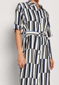Abito a camicia con righe nere, bianche e blu. Presenta maniche corte, colletto e una cintura annodata in vita. Tessuto dalla consistenza liscia.