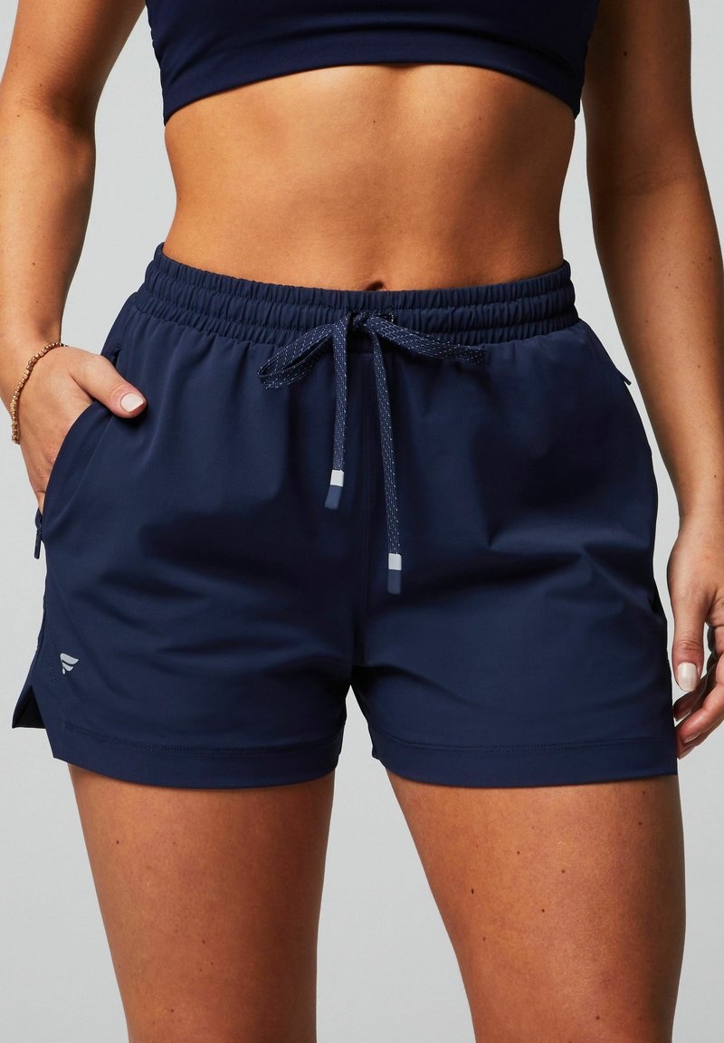 Marineblaue Sportshorts aus leichtem Fabric mit elastischem Bund, Kordelzug, seitlichen Taschen und einem kleinen Logo-Detail.