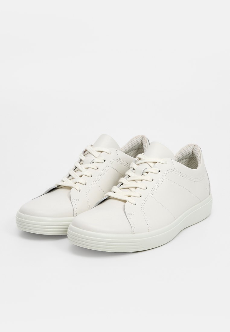 Ein Paar weiße, niedrige Schnürsneaker mit strukturierten Sohlen und gepolsterten Kragen auf einem weißen Hintergrund.