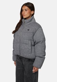 Szara kurtka puchowa z wysokim kołnierzem, z zamkiem błyskawicznym i boczną kieszenią. Posiada teksturowany materiał oraz subtelne logo na klatce piersiowej.