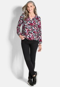 Langarm blouse met geometrisch patroon in bordeauxrood, zwart, lichtblauw en grijs; gecombineerd met zwarte strakke broek en zwarte sneakers.