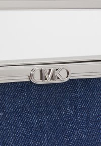 Silver metal clasp with the letters "MK" on a blue denim background, showcasing a sleek design and textured fabric.