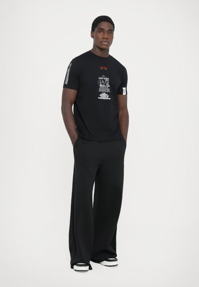 Black short-sleeve t-shirt with white graphic print and logo, paired with loose black pants. The outfit features white-accents on footwear.
