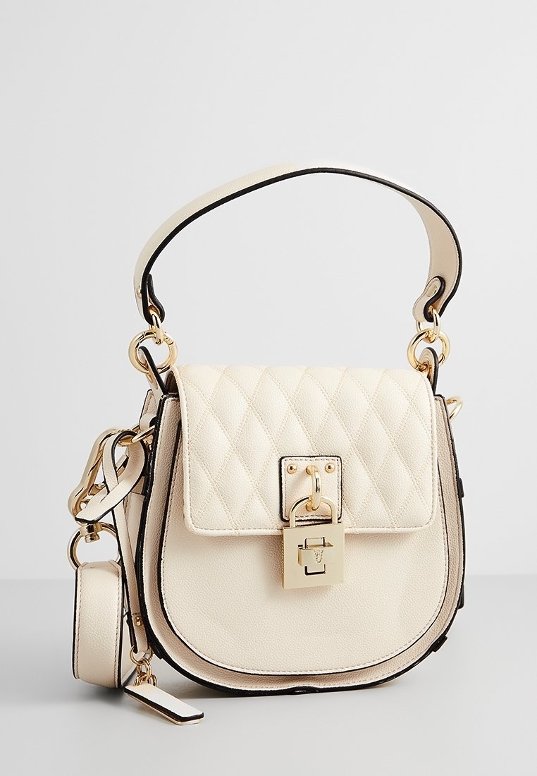 Sac à main matelassé crème avec rabat, quincaillerie dorée, détail de verrou et bandoulière amovible. Avec des finitions noires et une texture en cuir lisse.