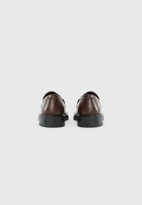 Chaussures en cuir marron avec une texture lisse, présentant un bout arrondi, un design minimal et un petit talon noir. Vue arrière mise en avant.