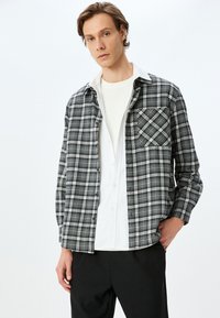 Rutig button-up skjorte i sort, hvid og grå med en brystlomme og krave over en hvid crew-neck skjorte. Blandingsstof af bomuld.